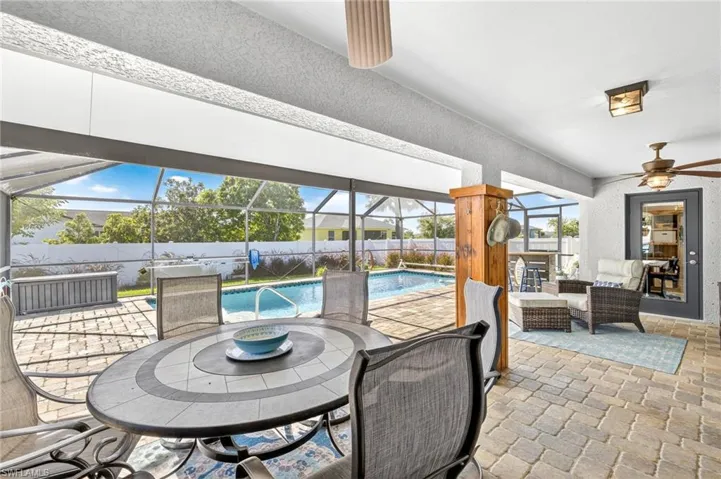 Fenced backyard with a ceiling fan, outdoor dining area, a patio area, and glass enclosure