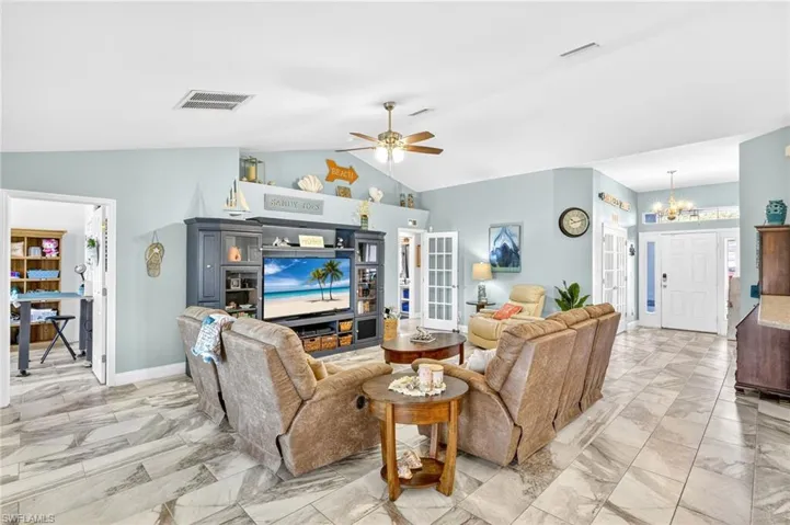 Living room with lofted ceiling, a chandelier, light marble finish floors, and a ceiling fan