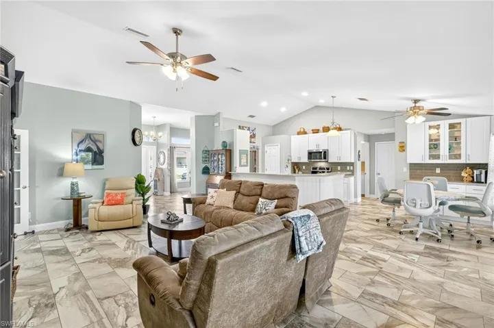 Living room with ceiling fan, lofted ceiling, light marble finish floors, and a chandelier