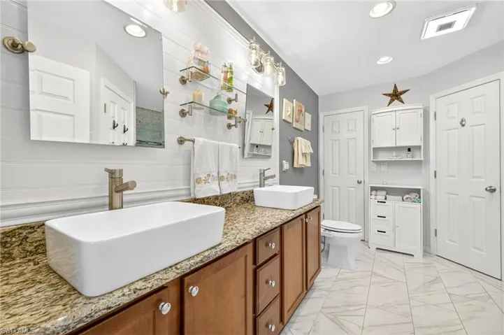 Full bath with double vanity, recessed lighting, and marble look tiles