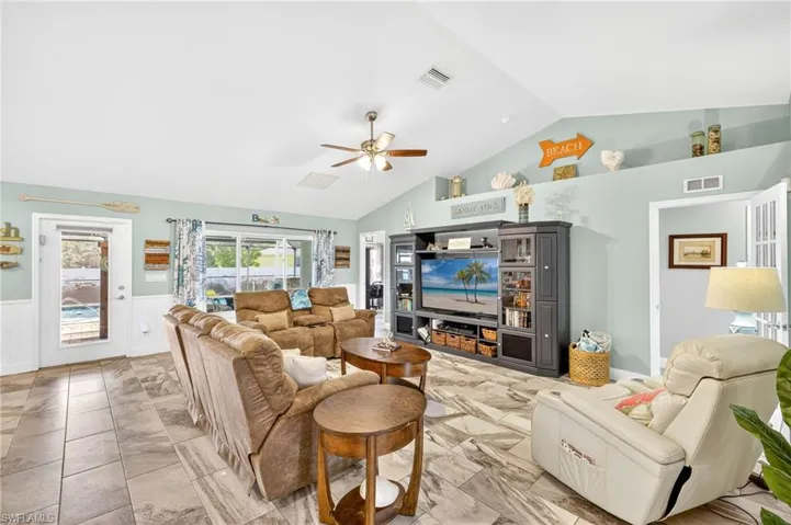 Living area featuring vaulted ceiling, a ceiling fan, wainscoting, and light marble finish floors