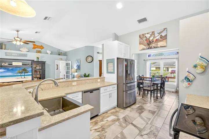 Kitchen featuring stainless steel appliances, light marble finish floors, white cabinets, ceiling fan, and high vaulted ceiling