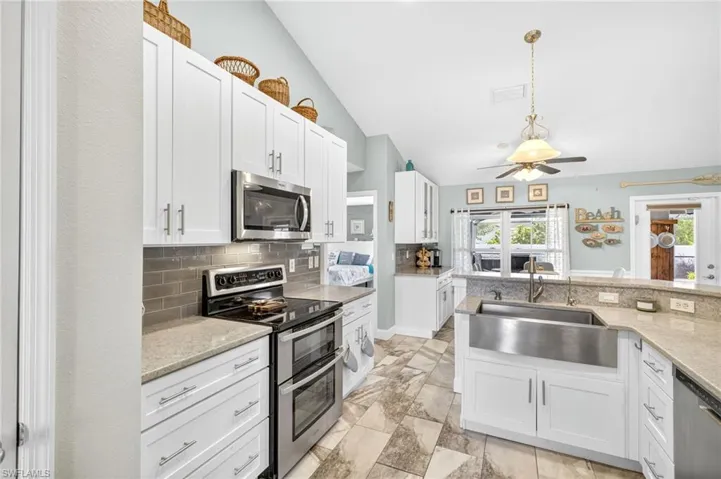 Kitchen with lofted ceiling, appliances with stainless steel finishes, backsplash, white cabinets, and ceiling fan