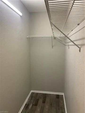 Walk in master closet with dark wood-type flooring