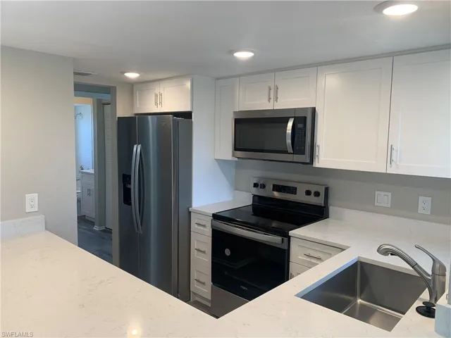 Kitchen with light stone countertops, stainless steel appliances, white cabinetry, and sink