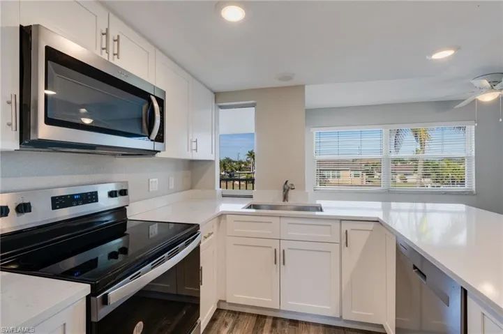 Kitchen featuring appliances with stainless steel finishes, white cabinets, light stone counters, dark wood-style flooring, and recessed lighting