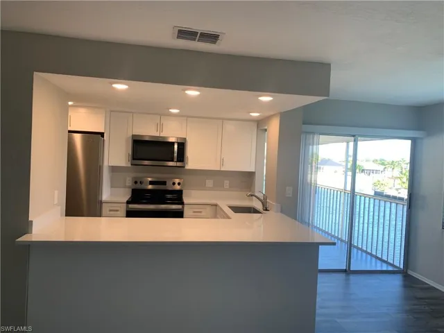 Kitchen with appliances with stainless steel finishes, white cabinetry, dark wood-type flooring, kitchen peninsula, and sink
