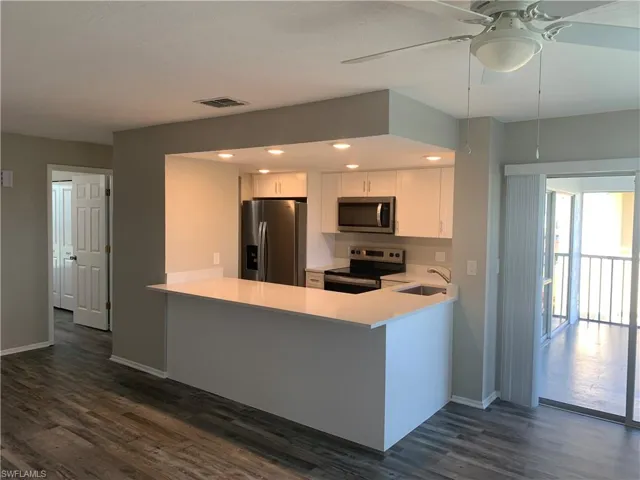 Kitchen featuring white cabinetry, dark wood-type flooring, kitchen peninsula, stainless steel appliances, and sink