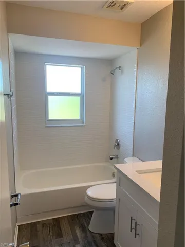 Full guest bathroom featuring hardwood / wood-style floors, tiled shower / bath combo, toilet, and vanity