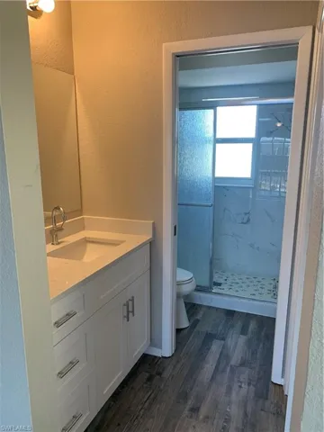 Bathroom featuring hardwood / wood-style flooring, vanity, toilet, and a shower with door