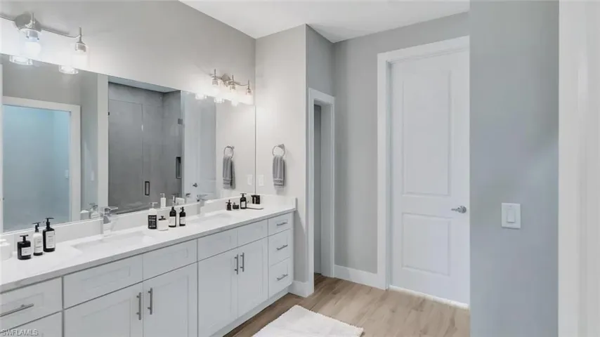 Full bathroom with double vanity, light wood-type flooring, and a stall shower