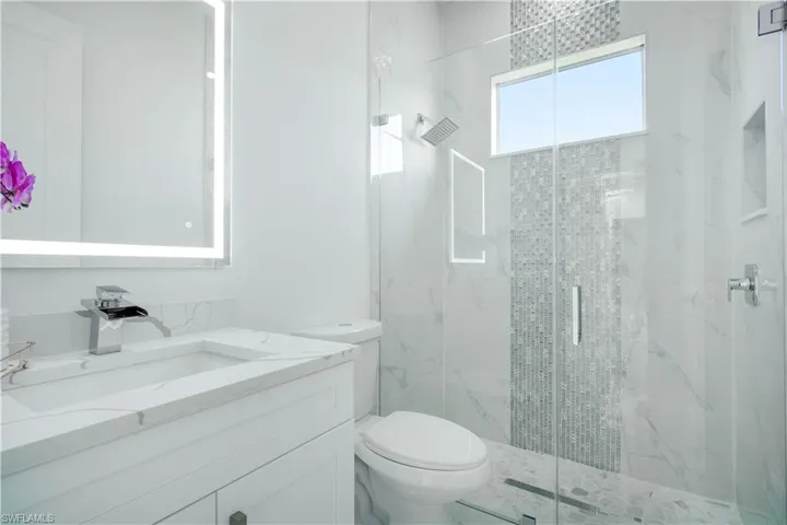 Bathroom featuring a shower with door, vanity, and toilet
