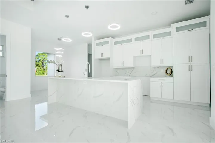 Kitchen with pendant lighting, light tile patterned floors, decorative backsplash, an island with sink, and sink