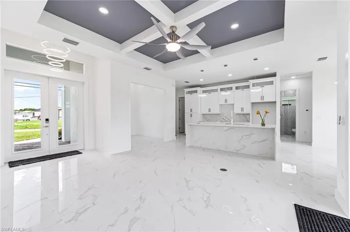 Unfurnished living room featuring ceiling fan, french doors, light tile patterned floors, coffered ceiling, and a tray ceiling