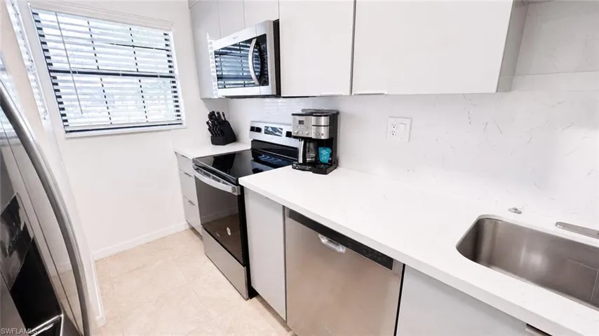 Contemporary kitchen featuring white cabinetry, stainless steel appliances, a white tile backsplash, a stainless steel sink, and light-colored flooring