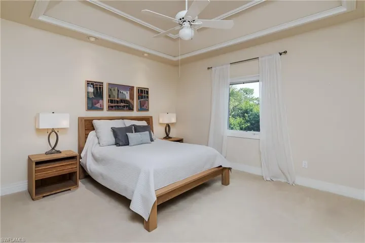 Bedroom featuring light colored carpet, a tray ceiling, and a ceiling fan
