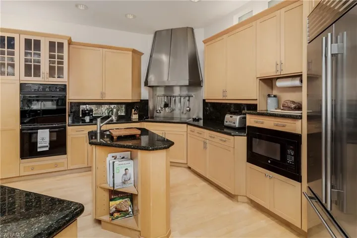 Kitchen with black appliances, wall chimney range hood, light brown cabinets, backsplash, and recessed lighting