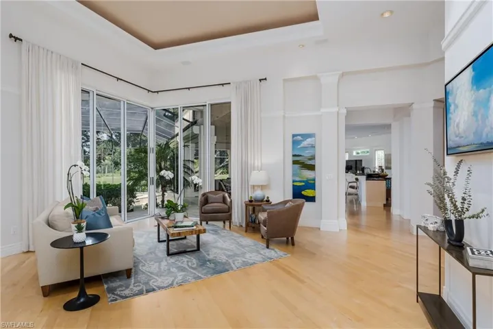 Sitting room with light wood-type flooring, decorative columns, and a raised ceiling