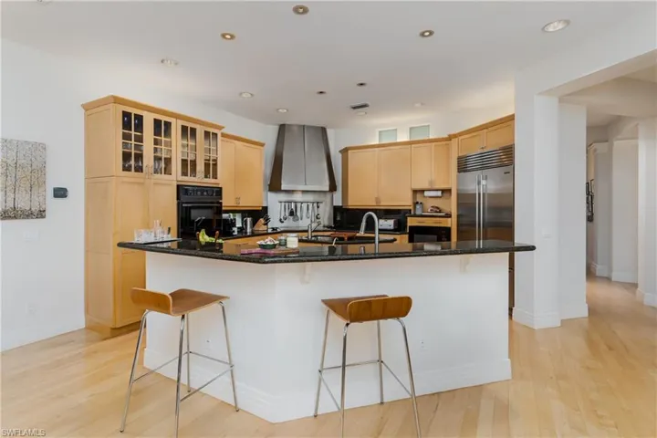 Kitchen with wall chimney range hood, oven, light brown cabinets, stainless steel built in refrigerator, and a kitchen breakfast bar