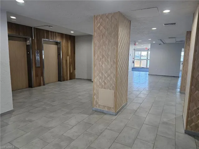 Corridor featuring a textured ceiling, elevator, and wooden walls