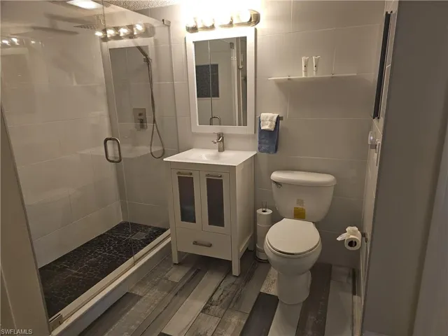 Remodeled Full Bathroom with vanity, toilet, a walk-in shower with frameless glass door, and wood plank style tile floors.