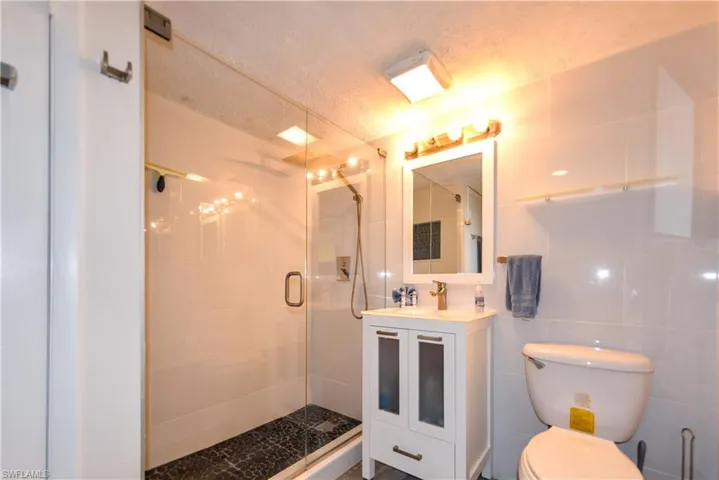 Bathroom with a shower with door, a textured ceiling, toilet, tile walls, and vanity
