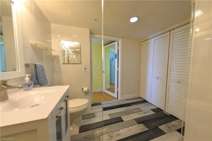 Bathroom with vanity, wood plank tile  flooring, a textured ceiling, and lots of closet storage.