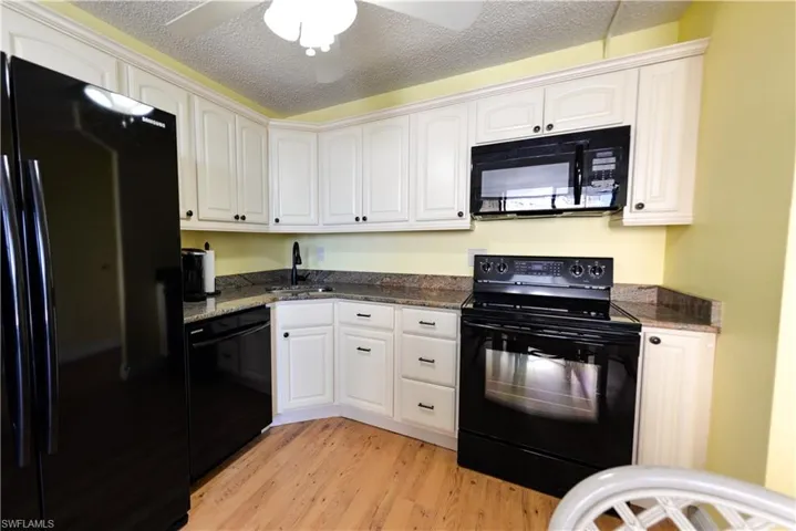 Kitchen featuring black appliances, sink, a textured ceiling, white cabinetry, and light hardwood / wood-style floors