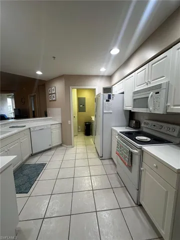 Kitchen with white appliances, light countertops, white cabinets, light tile patterned floors, and recessed lighting