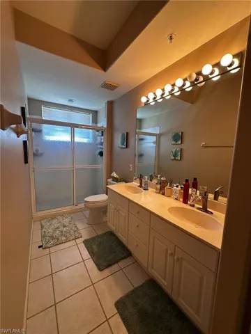 Bathroom with light tile patterned floors, a stall shower, and double vanity