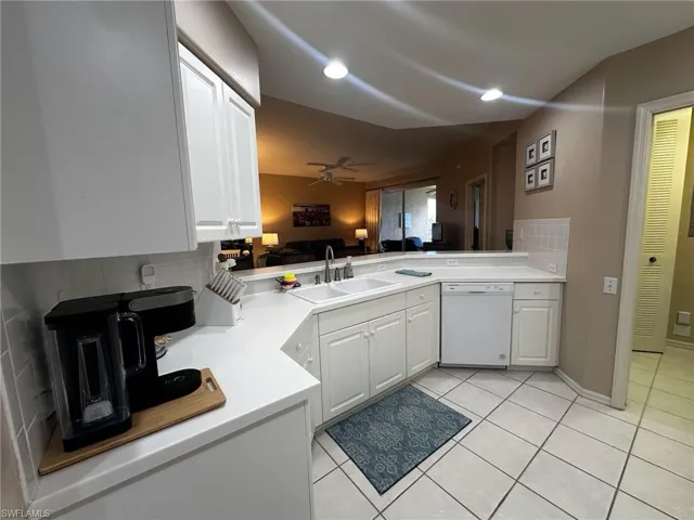 Kitchen with backsplash, light countertops, white dishwasher, light tile patterned floors, and a peninsula