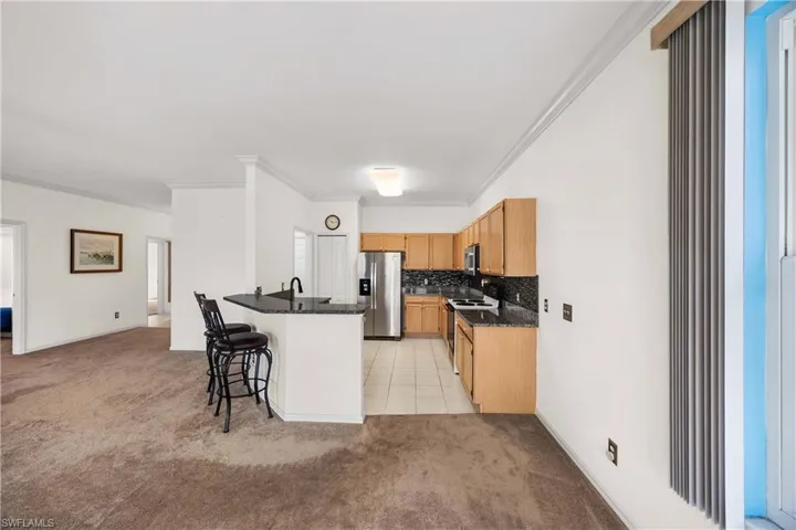 Kitchen featuring light carpet, stainless steel fridge, ornamental molding, a breakfast bar area, and dark stone countertops
