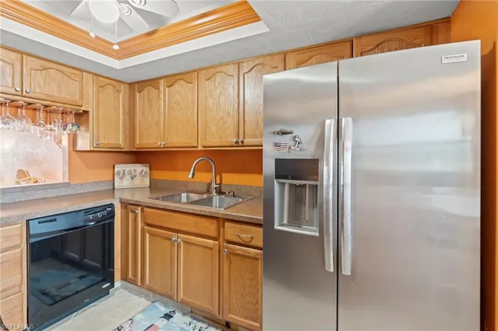 Kitchen featuring stainless steel fridge with ice dispenser, a raised ceiling, black dishwasher, light tile patterned flooring, and crown molding