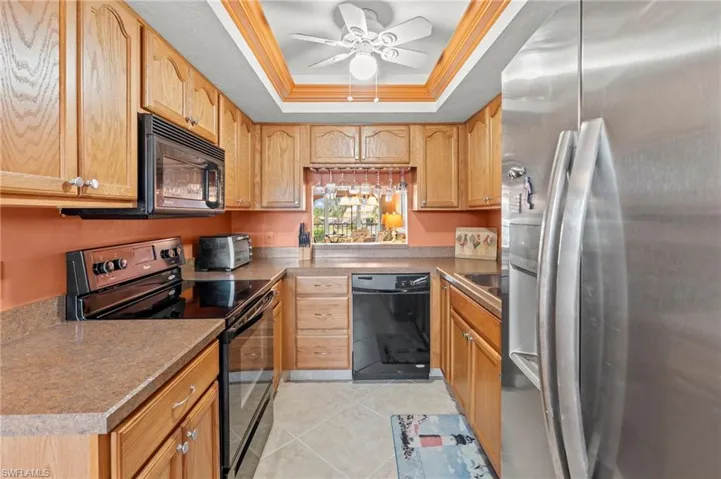 Kitchen featuring black appliances, a raised ceiling, light tile patterned floors, ceiling fan, and crown molding