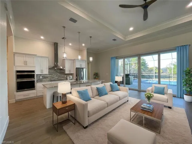 Living room with a tray ceiling, recessed lighting, a ceiling fan, ornamental molding, and light wood-type flooring