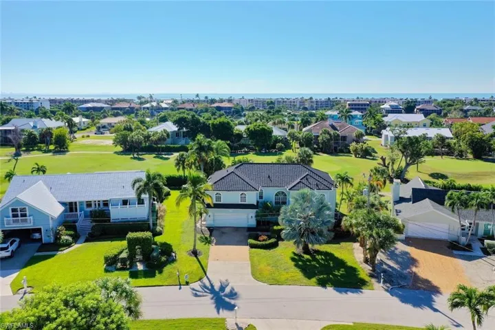 Two-story residence featuring a dark tile roof, multi-car garage, and expansive lawn, situated in a coastal community with open water horizon