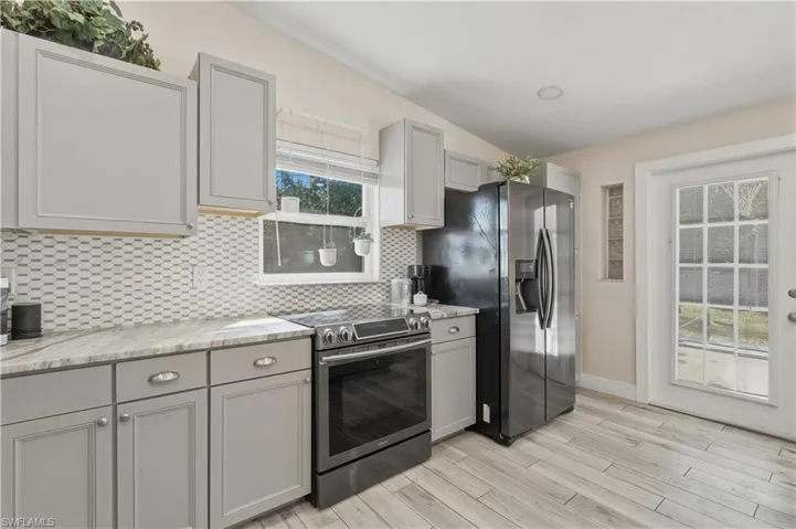 Kitchen with gray cabinetry, stainless steel appliances, light wood-style flooring, lofted ceiling, and decorative backsplash