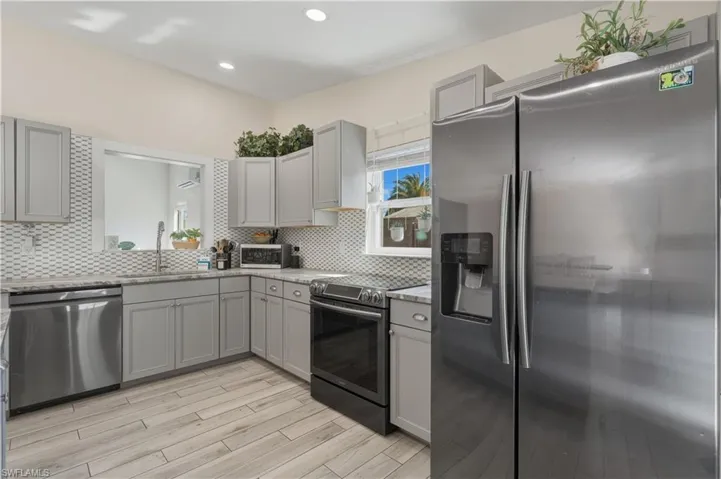 Kitchen with gray cabinets, stainless steel appliances, light wood-type flooring, light stone countertops, and recessed lighting