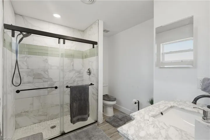 Bathroom featuring vanity, a marble finish shower, light wood-style floors, and recessed lighting