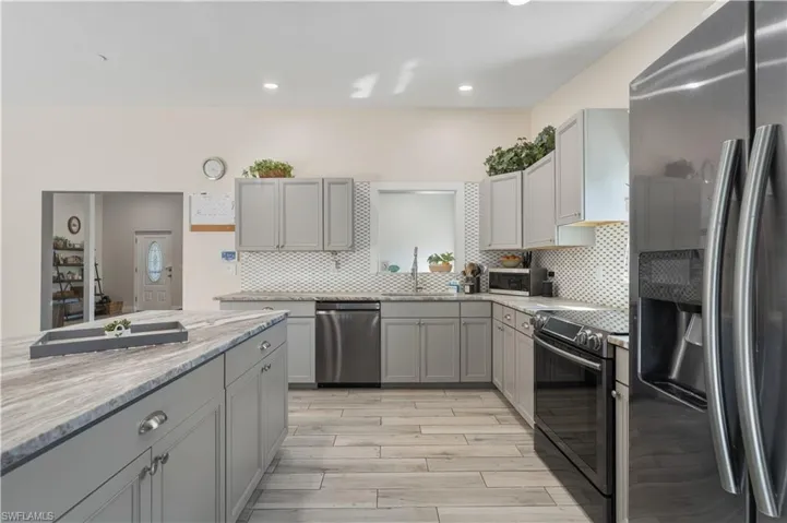 Kitchen featuring stainless steel appliances, gray cabinetry, backsplash, light stone counters, and light wood finished floors