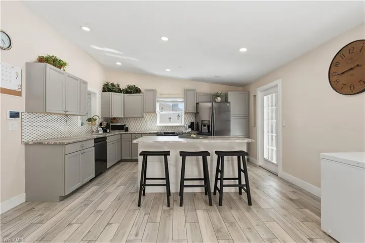 Kitchen featuring gray cabinets, a kitchen breakfast bar, decorative backsplash, vaulted ceiling, and stainless steel appliances