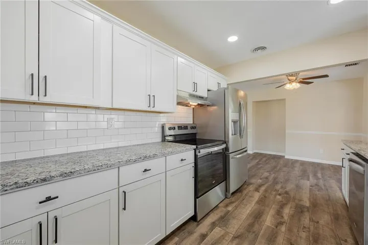 Kitchen featuring stainless steel appliances, tasteful backsplash, white cabinetry, light stone counters, and dark wood-style flooring