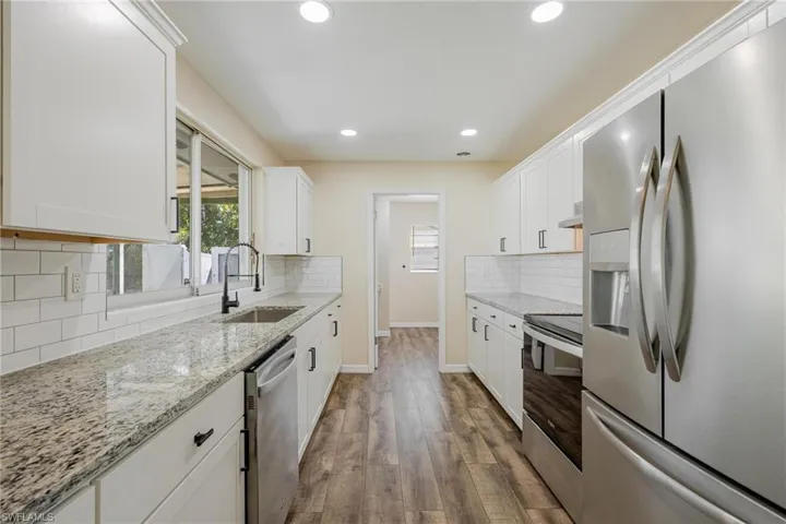 Kitchen featuring appliances with stainless steel finishes, white cabinetry, light stone countertops, dark wood-style flooring, and recessed lighting