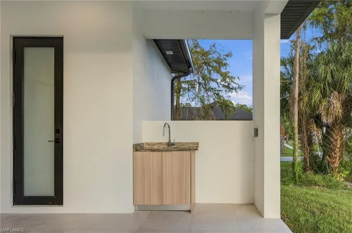 Covered outdoor patio featuring a wet bar with stone-surfaced countertop, sink, and wood-finish cabinetry, complemented by a matte black framed door with frosted glass panel
