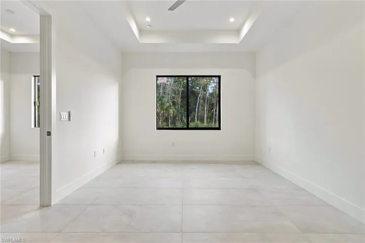 Tray ceiling with recessed lighting, large-format tile flooring, and black-framed windows