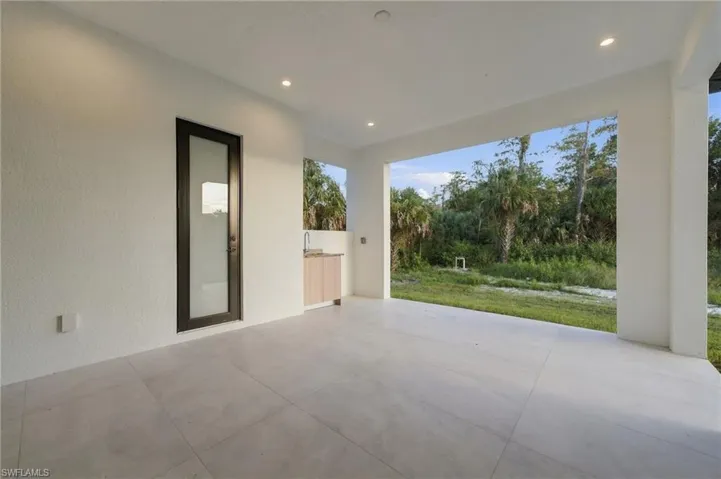 Covered patio featuring large-format porcelain tile flooring, recessed lighting, integrated outdoor cabinetry, and a full-height glass-paneled door