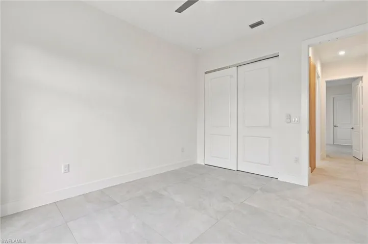 Neutral-toned tile flooring, white shaker-style sliding closet doors, and recessed ceiling lighting