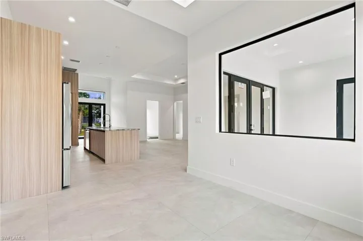 Open-concept interior featuring large-format tile flooring, recessed ceiling lighting, a kitchen island with wood-finish cabinetry, and a black-framed interior glass partition