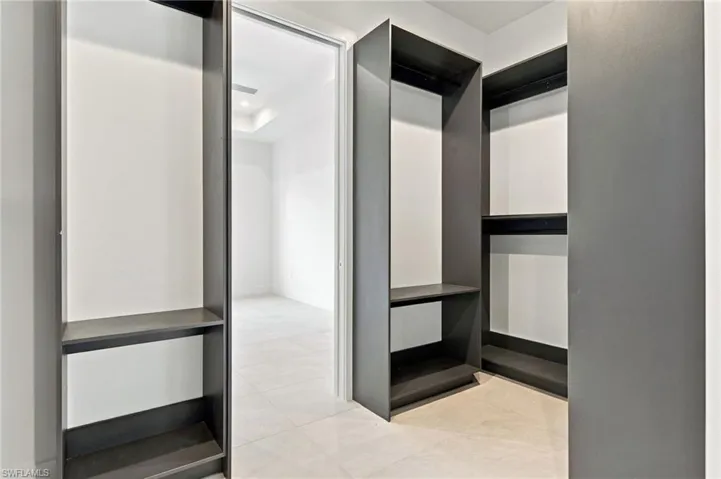 Walk-in closet featuring custom charcoal-toned floor-to-ceiling cabinetry, integrated shelving, and large-format tile flooring