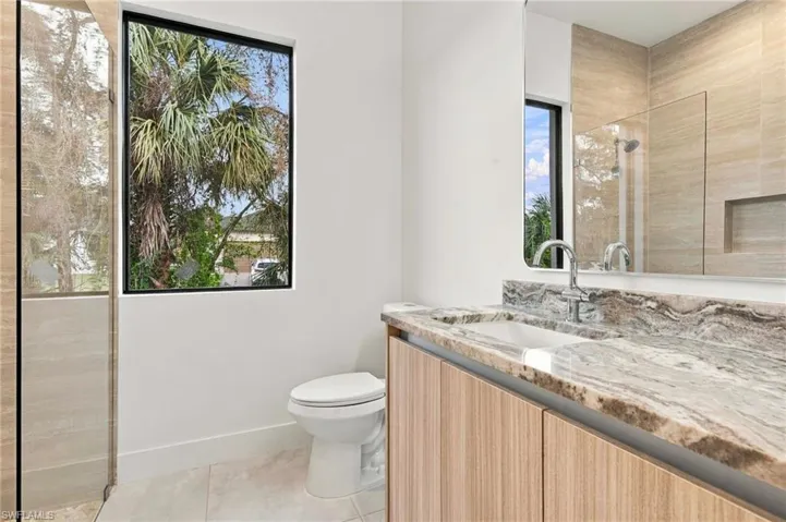 Bathroom featuring a wood-finish vanity with a natural stone countertop, large-format tiled shower enclosure, rectangular undermount sink, and polished chrome fixtures
